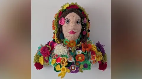 A colourful artwork made from crocheted wool, depicting a woman in flowery clothing and headdress.