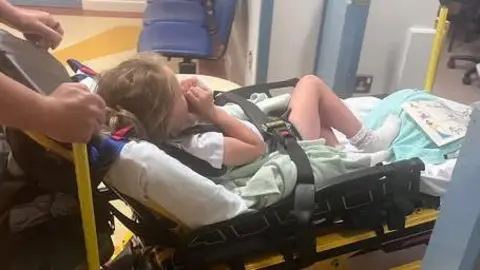 Family handout Young girl with blonde hair strapped onto a hospital stretcher