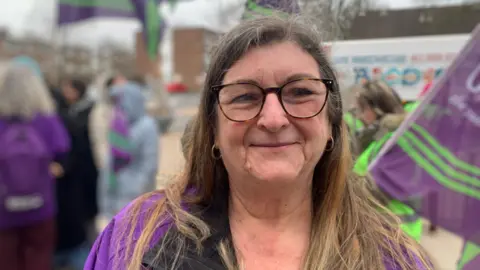 Woman with brown hair and glasses with purple union flags in background.