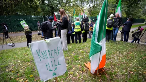 Apart from Woolwich Crown Court, Dizecap's PA Media supporters. In front of the photo, there is a poster of Kneecap Hill and Irish a three -color poster.