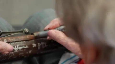 Joan Ramsay signing the rifle with a black Sharpie. Her face is away from the camera.