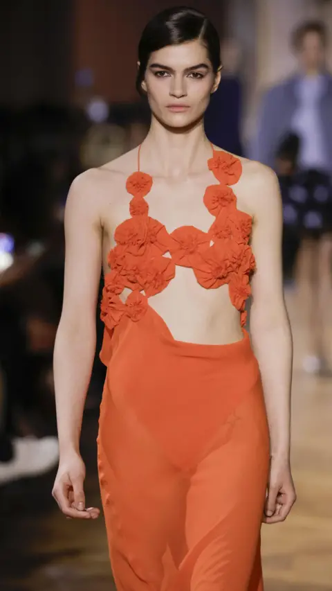 Getty Images A model wears a coral/red sheer dress with a floral design and a cut-out waist section.