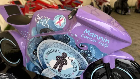 A close up of a purple sculpture with the Mannin Cancers Support Group logo