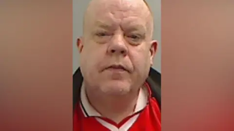 Mugshot of Scott. He is bald and clean shaven with a large round head.