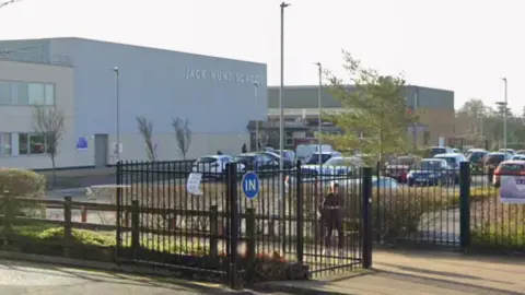 Google street view image of Jack Hunt- a big white building with Jack Hunt written on it in silver and black gates in front leading to a car park.