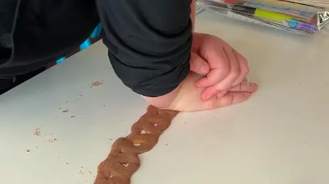 A child has their hands on a chocolate and caramel Curly Wurly trying to stretch it as far as possible.