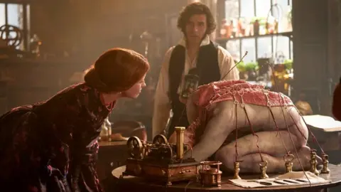 Netflix Oscar Isaac and Mia Goth in Frankenstein, looking at the monster being created