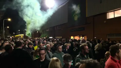 Norwich City fans outside their home stadium Carrow Road. Some have let off green smoke flares and some protest outside the entrance.