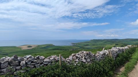 FRIDAY - A view over the Jurassic Coast and Kimmeridge in Dorset with fields and the sea in the distance. The photo is taken next to a dry stone wall