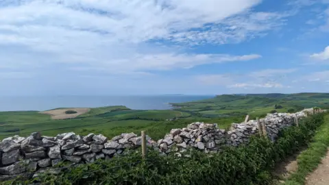 Eddie the Weather FRIDAY - A view over the Jurassic Coast and Kimmeridge in Dorset with fields and the sea in the distance. The photo is taken next to a dry stone wall