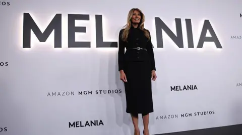 Samuel Corum / Getty Images Melania Trump stands in front of the title 'MELANIA' in large letters at the premier of the documentary film