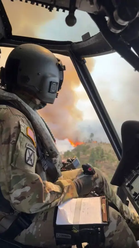 Reuters/Nevada National Guard An image taken from a video shows a National Guard member in a helicopter - in the background outside are flames and smoke billowing