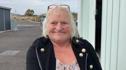 Henry Godfrey Evans/BBC Jane smiling at the camera. She is wearing glasses on her head and a black jacket and a top.