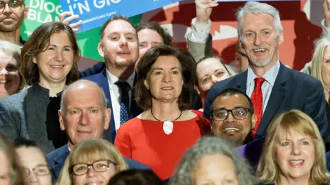 Athena A group of politicians and activists stood in a group on a stage, with First Minister Eluned Morgan stood in the middle.