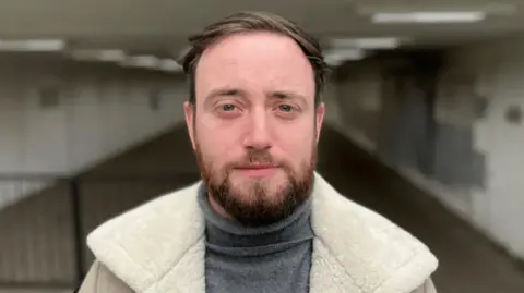 Jacob Dunne has a beard and is standing in a pedestrian subway