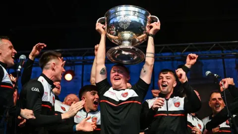 Getty Images Armagh goalkeeper Blaine Hughes holds the Sam Maguire cup above his head and celebrates alongside his teammates who are all cheering and wearing their Armagh kits at the Armagh team homecoming at the Carrickdale Hotel in Dundalk