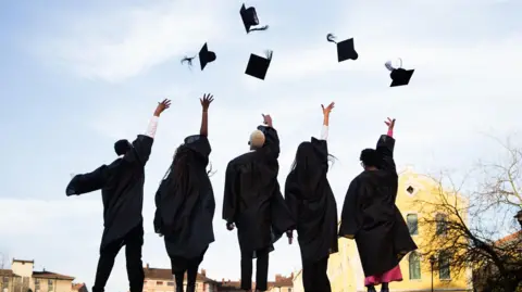Getty Images Graduates wearing black robes throwing mortarboards skyward, radiating excitement during commencement ceremony on bright outdoor setting 