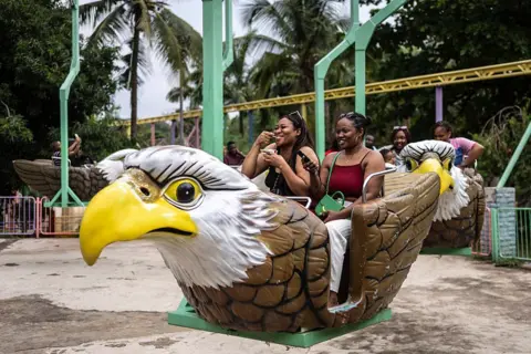 OLYMPIA DE MAISMONT / AFP / GETTY IMAGES Amusement park visitors talk, smile and laugh as they ride a bird-shaped carousel at Magic Land on 29 June.