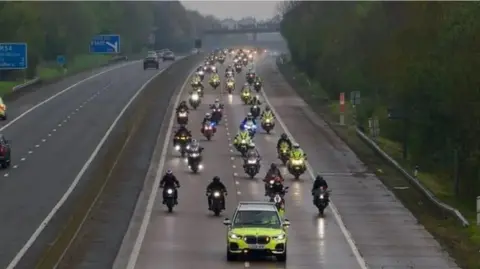 BBC A police car being followed by a convoy of motorbikes on the motorway