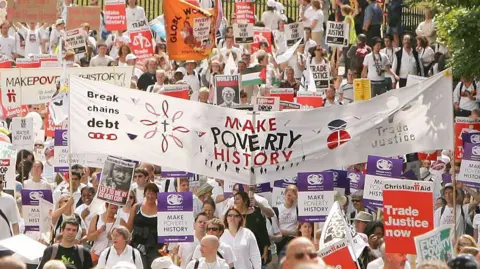 Getty Images A crowd of protesters walk through Edinburgh during the Make Poverty History march in 2005. They carry a large banner reading "make poverty history", "break the chains of debt" and "trade justice".