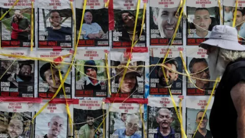 Reuters A man walks past a wall of posters in Tel Aviv, Israel, showing Israeli hostages being held by Hamas in Gaza (22 July 2024)