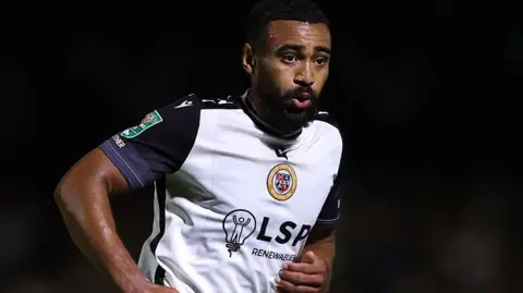Ashley Charles, wearing a white shirt with black sleeves, in action for Bromley