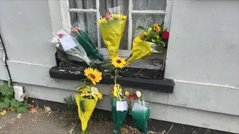 Richard Daniels/BBC Floral tributes near the scene of the fatal collision