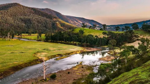 Getty Images A view of a river at sunset with green lush trees lining its banks and mountains in the background