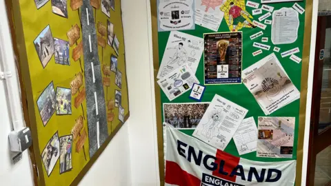 Worksheets can be seen on two school pin boards, with a large England flag at the bottom