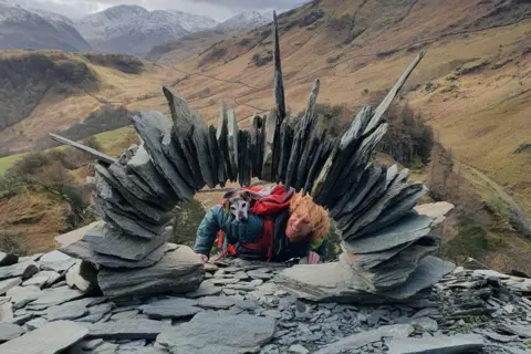 Rob Brown Slates piled in a semi circle with man and dog peering through the middle