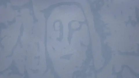 James Simpkins A close-up of one of the new shirts showing the ghost-like image of a face, one of the cave's carvings