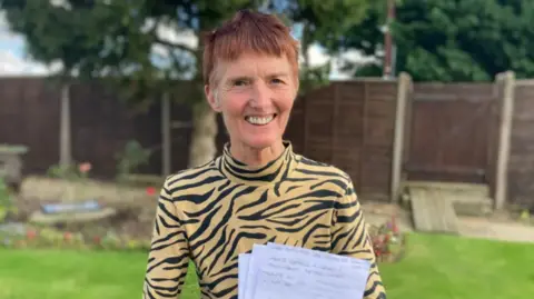 Tizi Hodson, formerly of Staverton in Gloucestershire, stands holding the letter that was returned to her after 48 years.