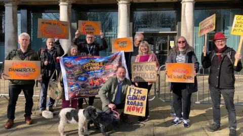 Pothole protesters with signs and a dog outside Nottinghamshire County Hall in West Bridgford