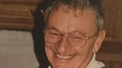 Claire Sharpe a man with grey hair smiles at the camera and is wearing glasses
