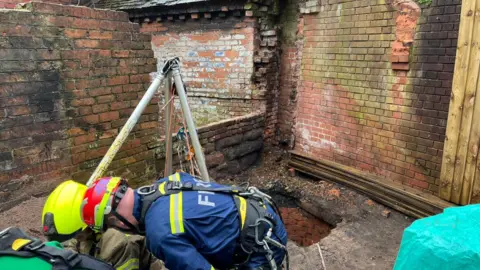Staffordshire Police Three men in emergency services gear are kneeling down on the floor, behind them there is an open well
