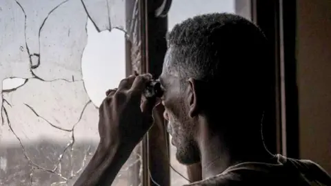 A Sudanese army soldier scans the frontline with binoculars in Khartoum North in December. He is looking out of broken window of a building.