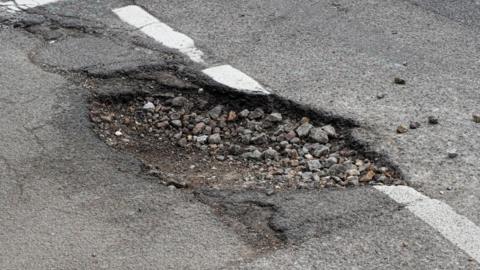 A pot hole at a junction in the road. There is gravel in the hole.