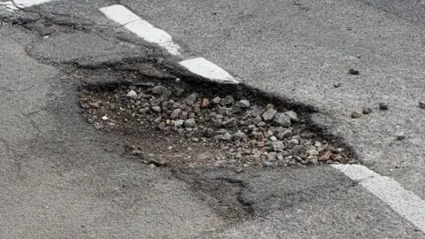 Getty Images A pot hole at a junction in the road. There is gravel in the hole.