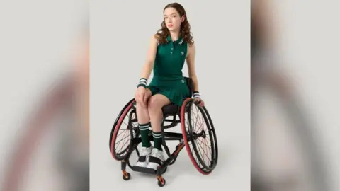FASHOT Alice Dyer has curly brown hair and is in her wheelchair. She's posing for a photo shoot wearing a dark green and white top and with a matching skirt, socks and wristbands. She has on white trainers