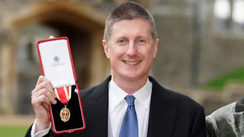 Sir Robert Chote holds up a medal in a red box