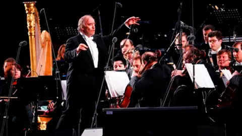 Russian conductor and Mariinsky Theater Artistic Director Valery Gergiev is surrounded by classical musicians on stage in Moscow in 2018. 