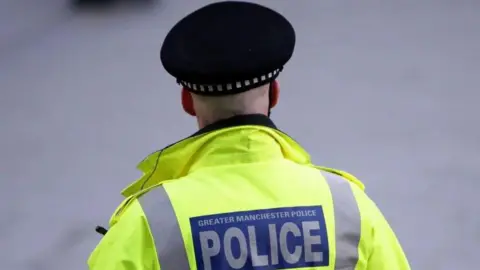 PA Media A Greater Manchester Police officer, pictured from behind, wearing a high visibility vest and police cap