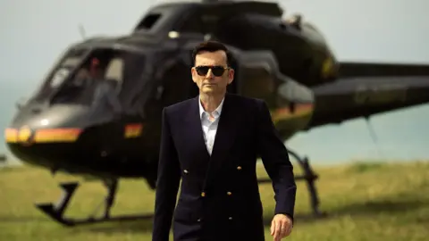 Disney Lord Tony Baddingham arriving via helicopter in a smart buttoned blazer