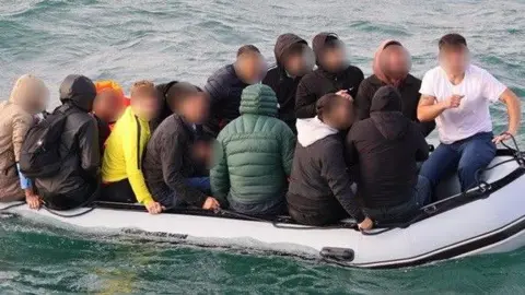 A close up of a packed dinghy taken shortly before it was intercepted in the English Channel. The man small boat is carrying 18 adults and one child to the UK from France.