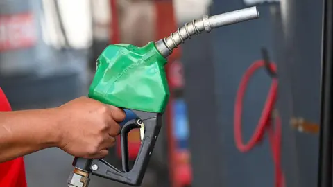 A person's hand holding a petrol pump. The pump is green.