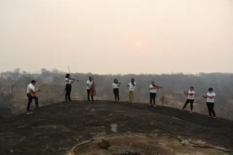 Claudia Morales / Reuters Members of the Misional Padre Martin Schmid Music School play their instruments on a hill destroyed by wildfire