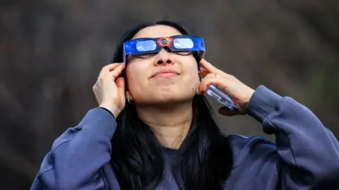 A woman observes the solar eclipse with an eclipse viewer, in New York in April 2024