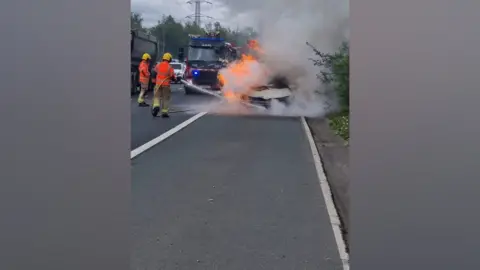 Other Firefighters extinguish a fire in a taxi on the M60 hardshoulder.