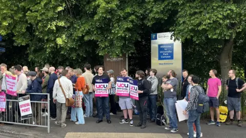 A line of students holding placards next to a University of Nottingham sign