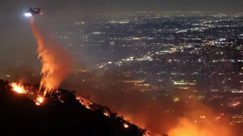 A firefighting helicopter drops water as the Sunset Fire burns in the Hollywood Hills